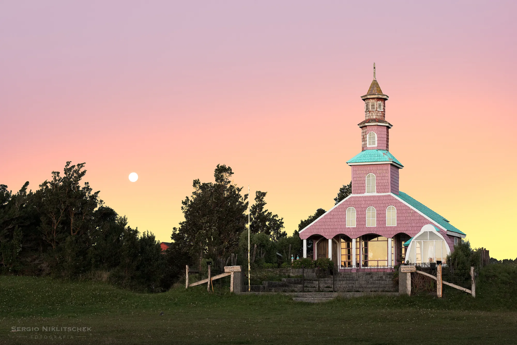 Capilla de tejuelas de Chacao Viejo, en Chiloé, al atardecer con la luna sobre los árboles