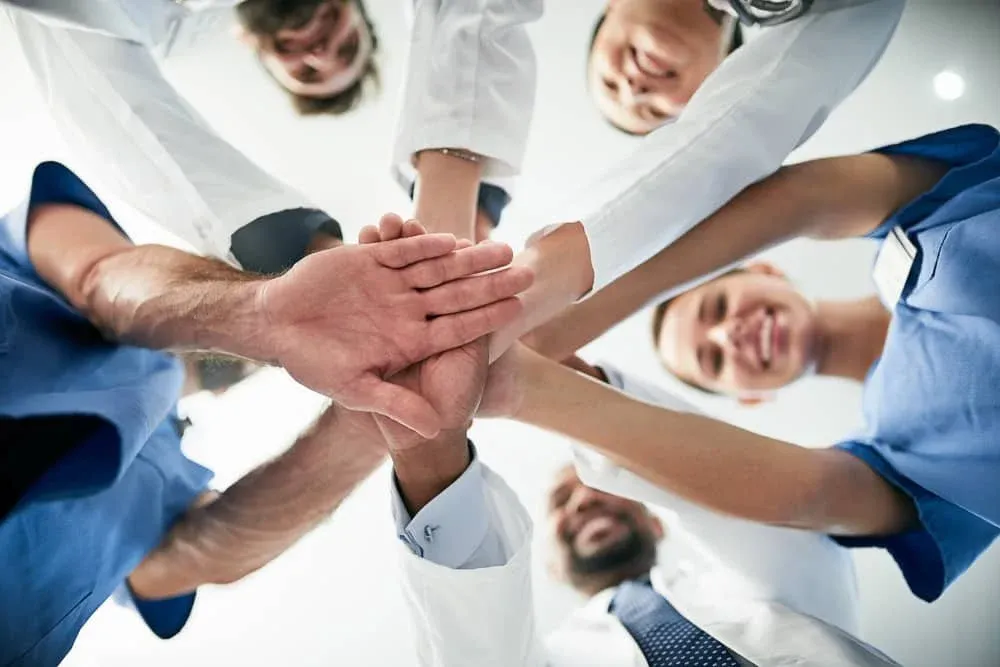 Equipo de profesionales de la salud uniendo sus manos en el centro, visto desde abajo