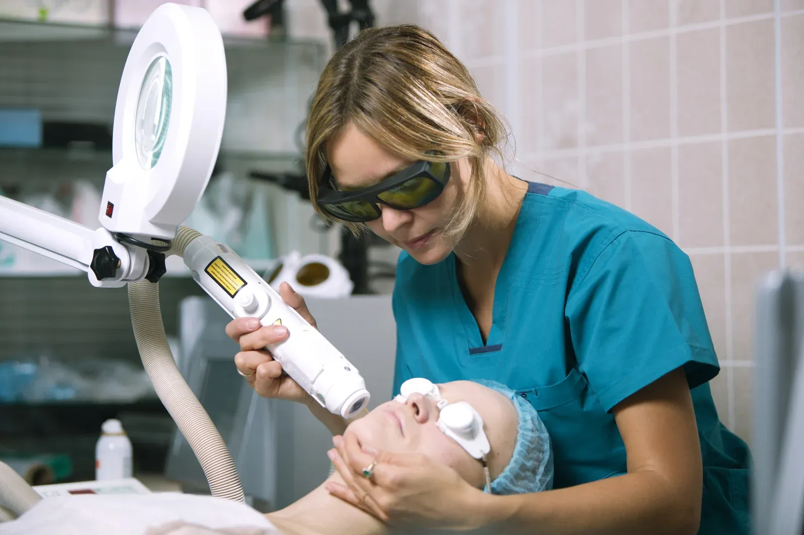 Profesional con gafas de protección aplicando un tratamiento con láser en el rostro de una paciente