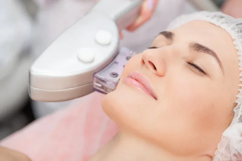 Mujer con gorro quirúrgico recibiendo un tratamiento facial con láser de rejuvenecimiento