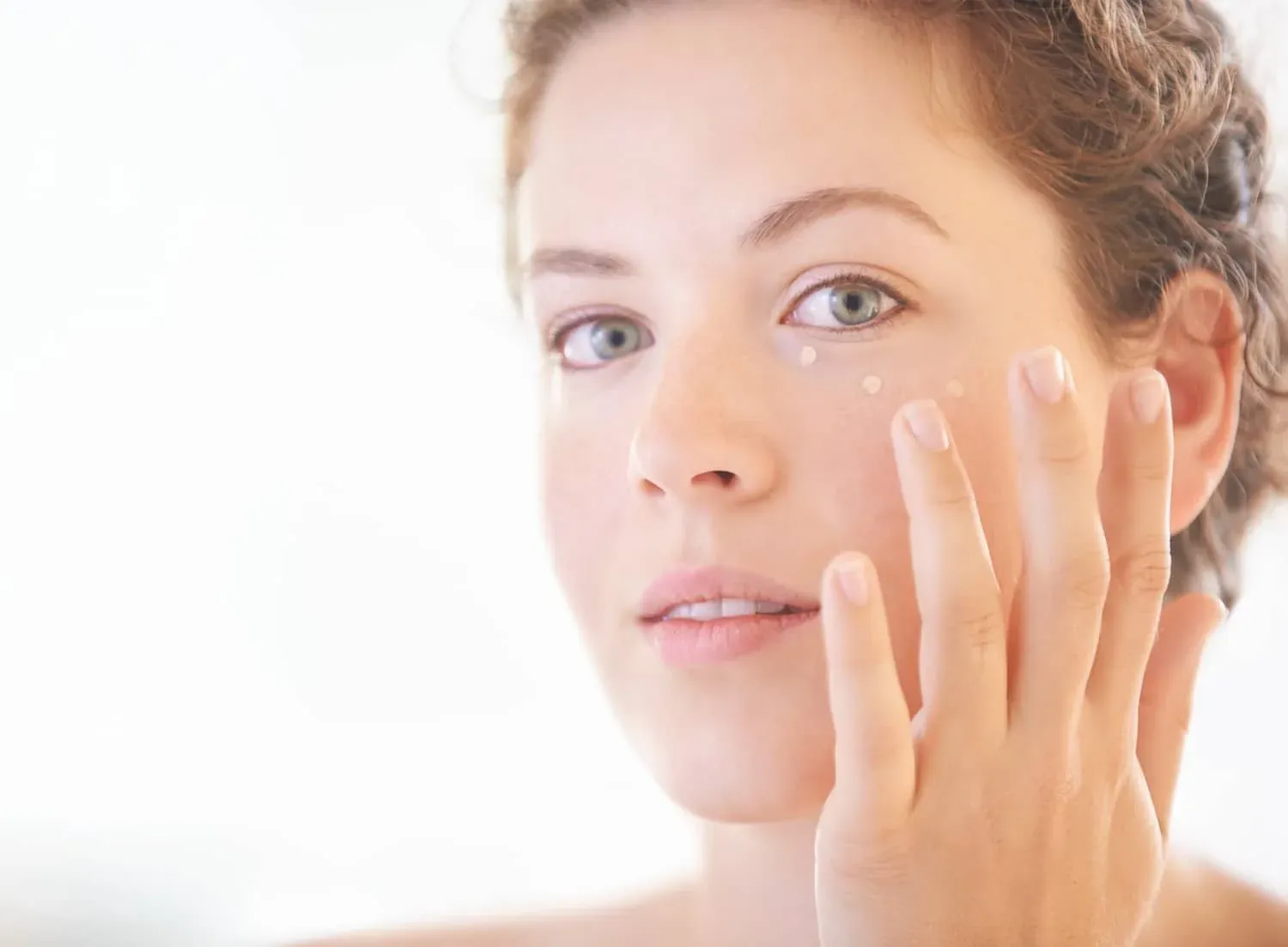 Mujer aplicando pequeños puntos de crema sobre la piel de la mejilla